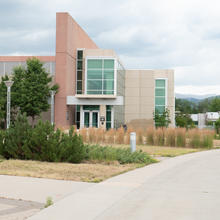 Angular office building in the center, with a sidewalk in front leading to the right and mountains in the background.