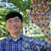 Ming Zheng stands outside smiling and holding a model of a nanotube made of a lattice of smaller tubes.