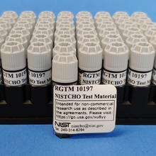 A rack of small vials with one pulled out in front for display, labeled "RGTM 10197 NISTCHO Test Material." 
