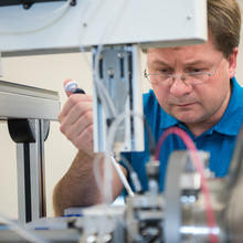 Alexander Grishaev leans over a counter full of scientific equipment, looking down at his work. 