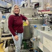 Susan Krueger poses in the lab, resting one arm on a large piece of scientific equipment. 