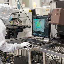 A worker in coveralls peers at a colorful computer screen next to a complicated piece of technical equipment. 