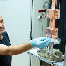 A man wearing latex gloves reaches out to adjust something on a cylindrical metal scientific device.