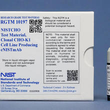 A small vial is displayed to the right of a square white box with various labels including "NISTCHO Test Material" and "NIST."