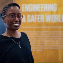 Jazalyn Dukes poses in front of a display that reads "Engineering a Safer World."