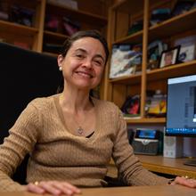 Ana Maria Rey sits at desk in an office and smiles for a photo.