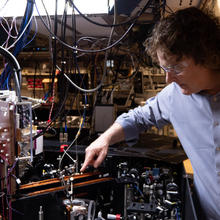 Andrew Wilson leans over a table packed with small devices in the lab. Loops of wire hang overhead and connect to other equipment. 