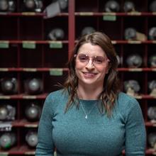 A woman in safety glasses stands between rows of metal cylinders.