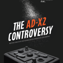 Red box at the top spilling out salt. Headline: The AD-X2 Controversy. Under head: car battery. List of producers, actors and interviewees, which can be found on Cast & Crew page of the site