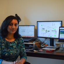 Nehika Mathur sits at a workstation with multiple computer monitors.