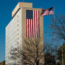 11 story building with an American flag draped down the side of the building and also an American flag on a pole.