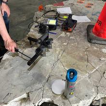 A worker uses a specialized device to tap on a large piece of broken concrete. 