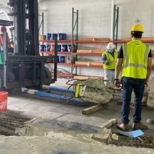 Two people in hard hats and safety gear stand looking at a large piece of concrete on a forklift. 