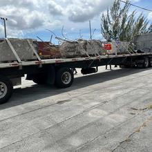 A long trailer parked outdoors holds pieces of concrete with broken metal bar around the edges.