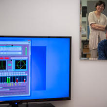 A mirror reflects Yoshi Ohno, seated, and Jane Li, standing, as they view a computer screen showing lighting data. 
