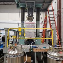 A large hydraulic press machine with vertical columns stands on a platform behind tanks labeled "Nitrogen."