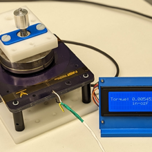 Tabletop scientific device includes circular magnets mounted on a black platform wired to a small screen with a torque readout.