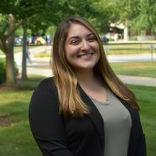 Headshot of a woman in front of trees wearing a green shirt and black cardigan