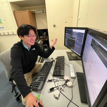 Morgan Ko sits at a desk with a computer and two monitors, smiling and gesturing as he speaks. 