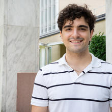 Navid Misaghian stands smiling outside a large building on the NIST campus. 