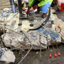 A slab of concrete with ragged edges sits on a warehouse floor as researchers use equipment to extract core samples. 