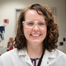 Wearing safety glasses and a lab coat, Jerilyn Izac poses for a portrait in the lab