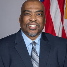 Essex Brown poses for a head shot with an American flag in the background.