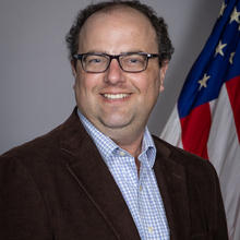 Jeremy Lawson poses for a head shot with an American flag in the background.