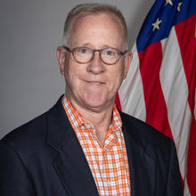 James Schufreider poses for a head shot with an American flag in the background.