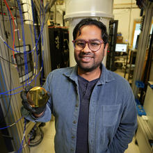 Akash Dixit stands in the lab surrounded by server racks and wiring, holiding a reflective disk. 