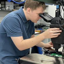 Drew Borders leans forward to look into a microscope attached to a large frame.