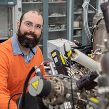 Trey Diulus poses sitting in the lab with a large, complex scientific instrument in the foreground.