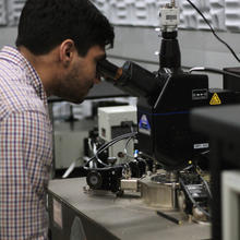 Samuel Márquez González leans forward to look through a microscope in the lab. 