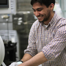 Samuel Márquez González grins as he stands in the lab handling scientific equipment. 