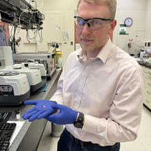 Brad Sutliff displays small circles of plastic on his gloved palm as he stands in the lab wearing safety glasses. 