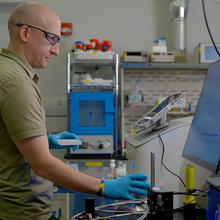 Thomas Forbes wears safety glasses as he looks at the screen attached to a piece of equipment in the lab. 