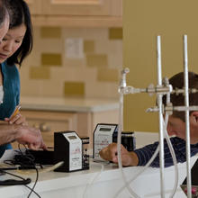 Three researchers stand and look down to examine various small electronics and wiring on a kitchen counter.