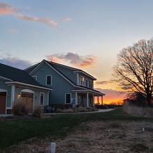 The net-zero house and nearby trees are silhouetted against the setting sun. 