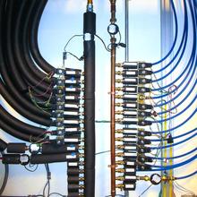 Two parallel vertical pipes are each connected to many others leading off horizontally in opposite directions. The connecting pipes on the left are insulated with black foam.