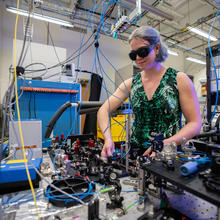 Alejandra Collopy wears safety glasses as she works the lab. She is surrounded by various pieces of equipment and many hanging wires. 