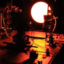 A circular light shines in a darkened lab, with equipment and wiring in the foreground.