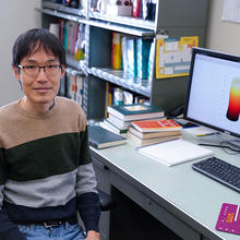A researcher poses at his desk with a computer screen showing a cylindrical model of an esophagus. 