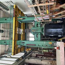 A two-story metal testing apparatus stands inside a high-ceilinged lab space filled with other equipment and scaffolding. 