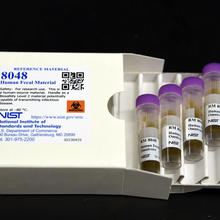 A white box labeled "8048 Human Fecal Material" lies open, with a tray of four plastic vials pulled out. 