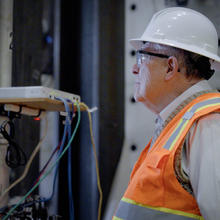 A man in a hard hat and high-vis vest looks at something happening out of the frame. 