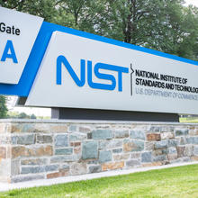 Outdoor entry sign with trees in background reads "NIST U.S. Department of Commerce, Gate A."