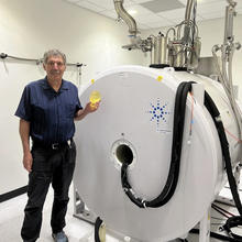 Stephen Russek poses in the lab holding a small model of a human head and standing next to the large cylinder of an MRI machine.