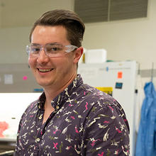 Sam Schaffter wears safety glasses as he poses smiling in the lab.