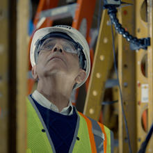 Photo of structural elements surrounding man with helmet and glasses looking up 