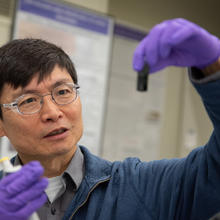 Researcher Ming Zheng looks with interest at a small vial he is holding up in front of him. 